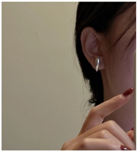 Close-up of minimalist matte silver S925 drop earrings worn by a model on ear lobe