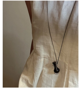 Dettaglio di una lunga collana in argento minimalista con ciondolo a bottiglia su lino