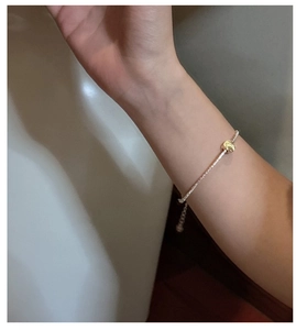 Detail of silver chain bracelet with gold knot design on wrist with adjustable clasp