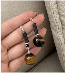 Detail of asymmetrical beaded earrings featuring brown tiger eye stones and silver hooks