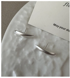 Macro shot of minimalist matte S925 sterling silver curved bar earrings on white ceramic
