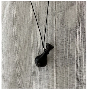 Dettaglio della collana con ciondolo a vaso nero su sfondo di lino materico