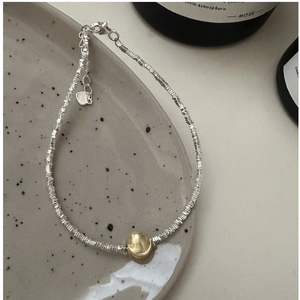 Detailed macro of S925 sterling silver beaded bracelet with gold center bead on ceramic tray
