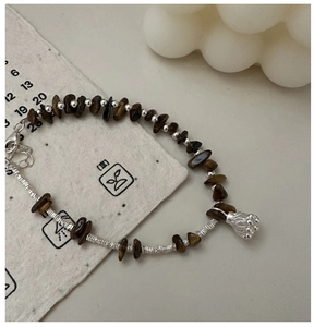 Detail of tiger eye stone bracelet with silver lotus pendant on vintage paper backdrop
