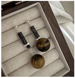 Macro detail of asymmetric S925 silver earrings with tiger eye and obsidian beads