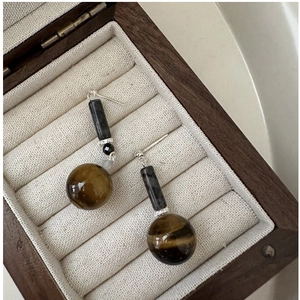 Macro detail of S925 silver earrings with tiger eye stone and dark cylindrical beads