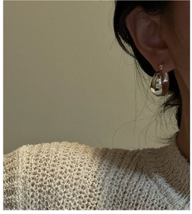 Macro shot of minimalist thick silver hoop earrings worn on a model's ear with soft light