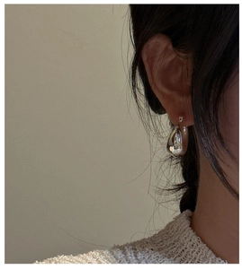 Close-up of a large silver hollow teardrop earring worn on a model's ear