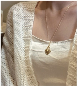 Detail of vintage heart pendant necklace in gold finish worn on a white cardigan
