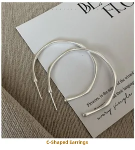 Detail of matte S925 silver C-shape hoop earrings with brushed texture and wavy design