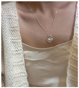 Macro detail of silver heart pendant featuring vintage sunburst texture on sweater chain