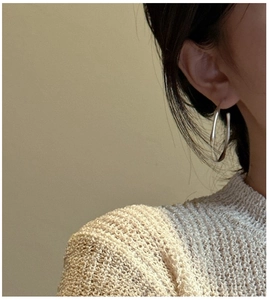 Macro shot of large matte silver hoop earring worn by a model in beige knitwear