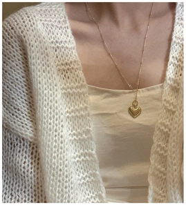 Detail of golden heart pendant necklace with ribbed texture on white sweater