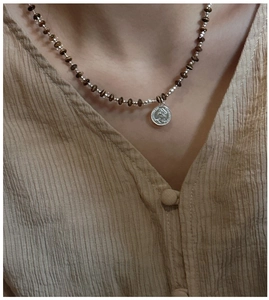 Detail of vintage silver coin pendant necklace with dark brown beads on a linen shirt