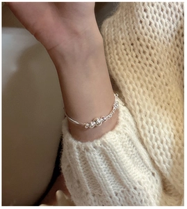 Detailed close-up of a triple-layered silver bead bracelet worn over a knit sweater