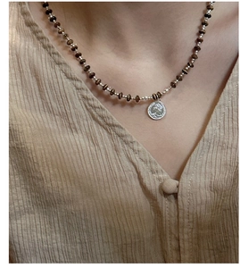 Macro shot of S925 silver coin pendant with brown beads on a layered v-neck garment