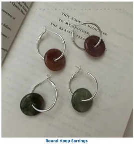 Close-up of S925 silver hoop earrings with dark red and green stone charms on a book