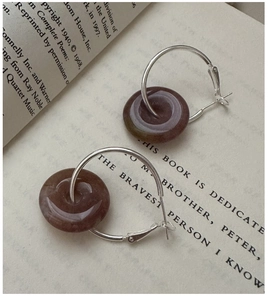 Macro detail of S925 silver hoop earrings with purple marble stone charms on a book