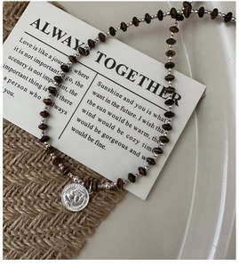 Macro shot of silver metal beads and brown disk-shaped beads with a silver coin pendant