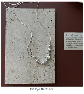 Artistic display of a silver snake chain necklace with cat eye beads on beige stone
