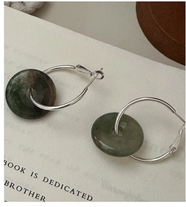 Close-up of S925 silver hoop earrings with dark green round pendants on vintage book pages