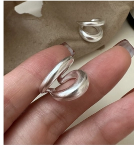 Détail d'un ear cuff minimaliste en argent mat avec design ondulé porté sur l'oreille