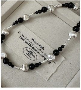 Macro shot of silver metal balls and black onyx beads necklace on a linen gift box display