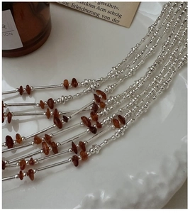 Detailed close-up of S925 silver beaded necklace with brown crystals on ceramic tray