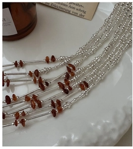 Detail of beaded S925 silver necklace with reddish amber stones on a white tray