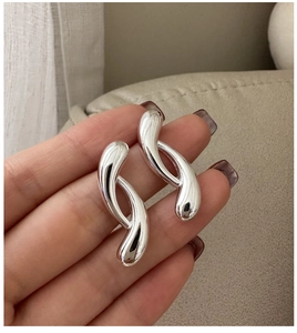 Close-up of fluid abstract silver earrings held in hand to show size and glossy texture