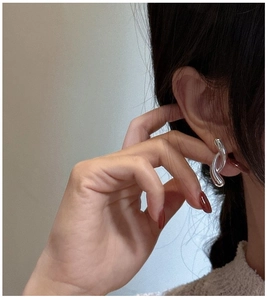Detail view of silver S925 cross-curved double loop earrings worn on a female ear