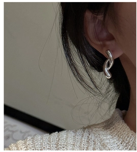 Macro shot of silver S925 curved cross earrings worn on ear in a minimalist style