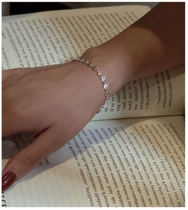 Close-up of minimalist S925 sterling silver heart bracelet on wrist with book background