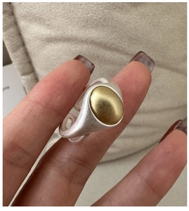 Detail of a matte silver adjustable open ring featuring a gold oval metal centerpiece