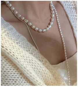 Detail of layered S925 silver necklace with baroque pearls on cream knitwear