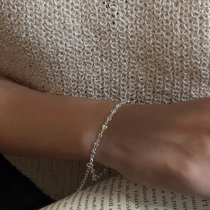 S925 sterling silver heart link bracelet on a wrist against a beige knitted sweater background