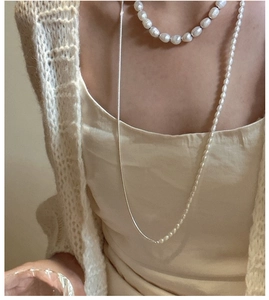 Detail of layered S925 silver pearl necklace with knot design on elegant beige cardigan