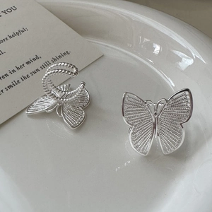S925 sterling silver butterfly ear cuffs with intricate hollow design on a ceramic plate