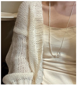 Close-up of S925 silver knot necklace with pearls and snake chain detail on a beige cardigan