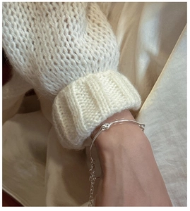 Detail of S925 sterling silver knotted bracelet on a soft knit sweater sleeve