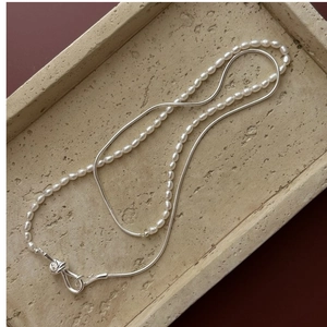 Detail of S925 silver knot clasp with pearl strand and snake chain layers on stone tray