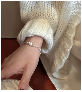 Detail of silver S925 beaded bracelet with a crescent charm worn over a cream knit sweater