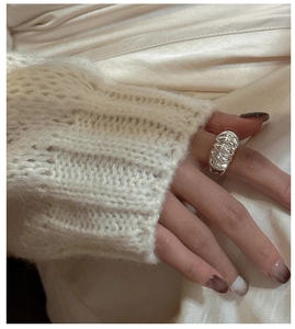 Detailed close-up of a wide hollow silver croissant ring on a finger with a cozy sweater sleeve