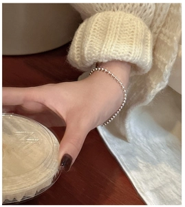 Minimalist S925 sterling silver beaded bracelet on wrist with a cozy knit sweater sleeve