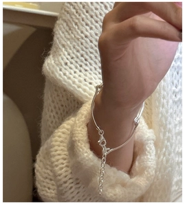 Detail of S925 sterling silver minimalist bracelet with lobster clasp on a white knit sleeve