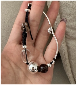 Detail of woven silver bracelet with metal beads, petal charm and hook closure
