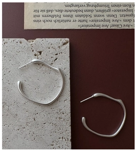 Detail von matten, unregelmäßigen Creolen aus Silber auf Stein- und Papierhintergrund