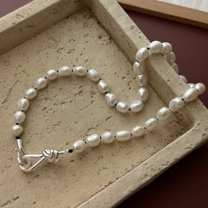 French vintage baroque pearl necklace with silver knot clasp on beige stone tray