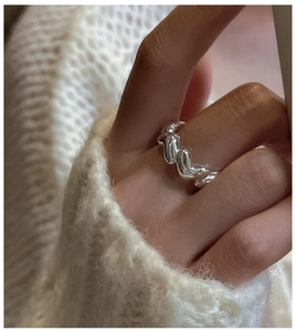 Close-up of wavy stacked silver ring on finger with white knit sweater background