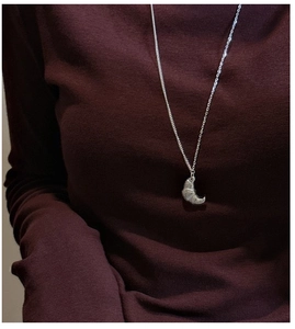 Detailed view of silver S925 croissant pendant necklace on a dark burgundy turtleneck top